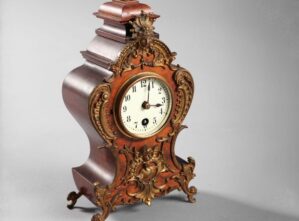 Ornate antique mantel clock with carved wood and gilded decorative accents. {{brizy_dc_image_alt imageSrc=